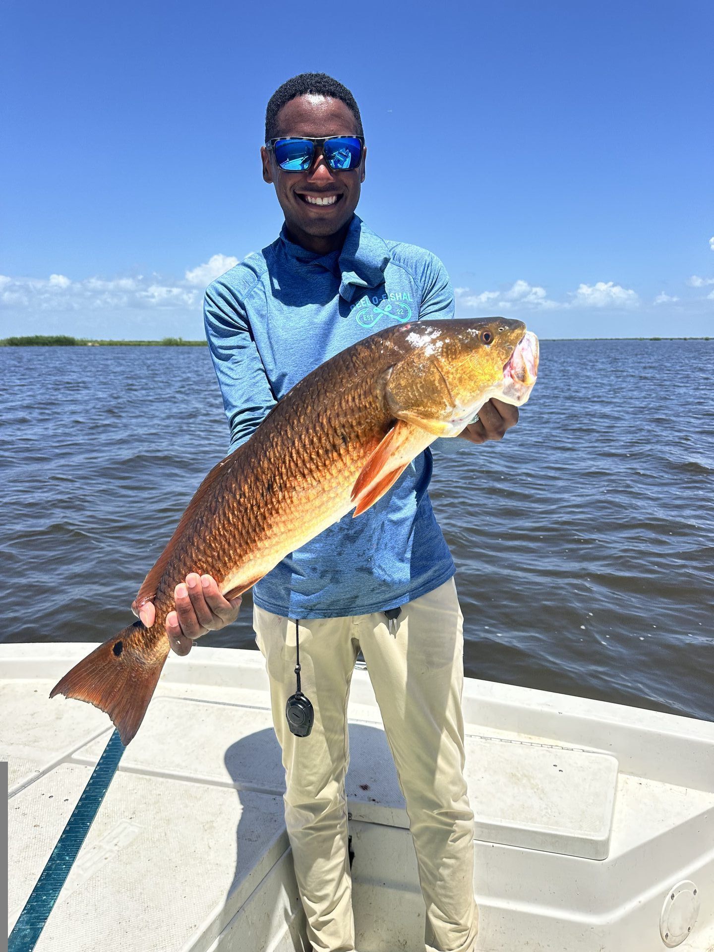 Captain Derrious Austin smiling and holding a large redfish on the water
